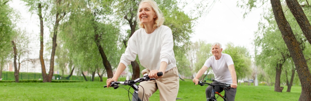 An elderly couple riding their bikes in the park.